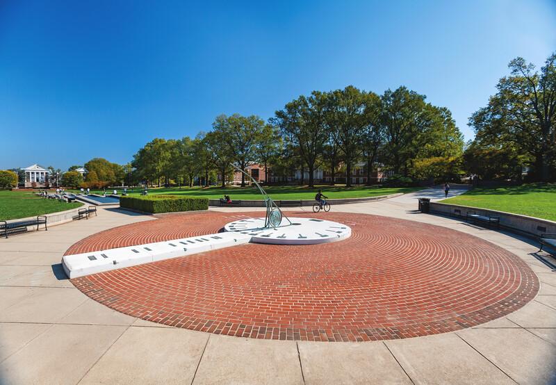Perspective of the Sundial with students walking, and a view of the Mall in the background, with blue sky and clouds.